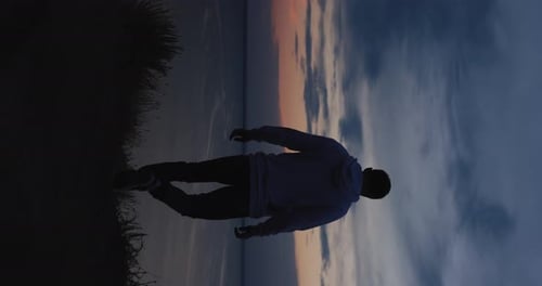 Silhouette eines Mannes, der am Abend auf einem Hügel spaziert Vertikales Video