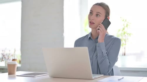 Woman Talking on Phone While Using Laptop in Office