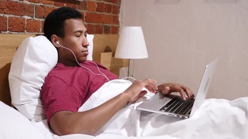 Young Adult Man Using Laptop in Bed