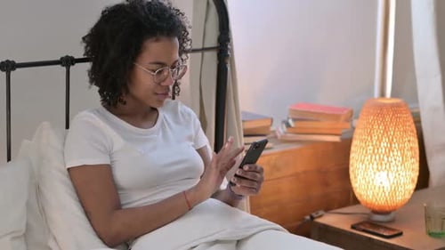 Woman Using Cellphone Relaxing in Bed at Home