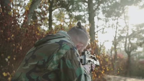 The Versatile View of Soldier Tracks the Object with a Rifle Sight at Forest