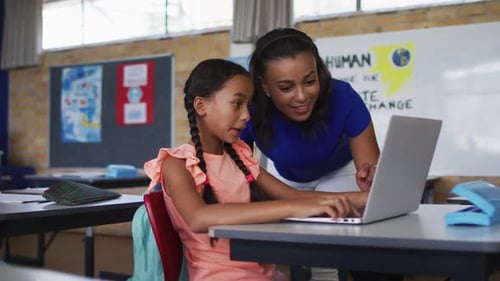 Teacher Helping Student with Laptop in Classroom