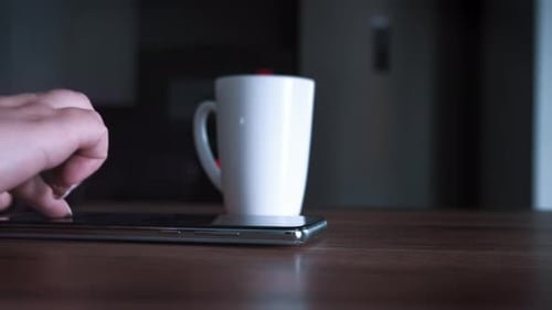 Close Up of Woman Hand Drinking Tea in the Kitchen and Using the Phone in the Evening