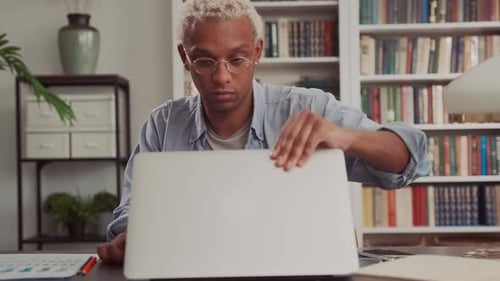 Young Adult Opens Laptop at Desk
