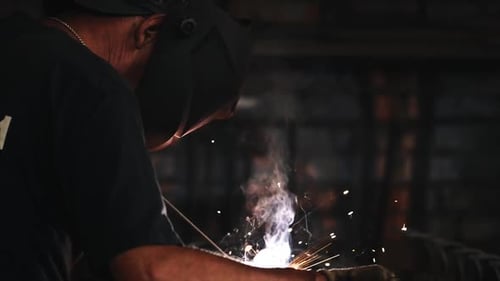 Welder in Protective Mask Makes Electric Arc Welding of Metal