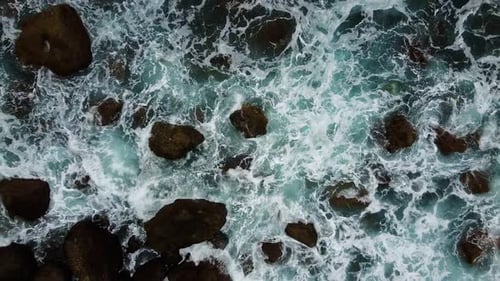 Aerial Top View Foamy Waves Break on Dark Rocks Near Beach