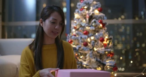 Woman Opens Gift by Christmas Tree in Apartment