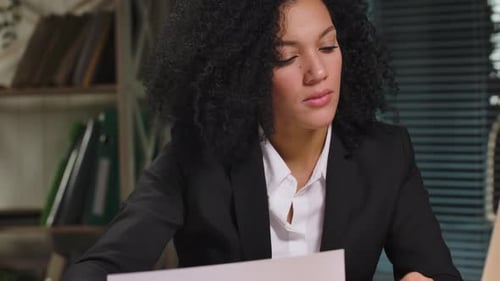 Serious Woman Reviews Graphs at Desk with Laptop