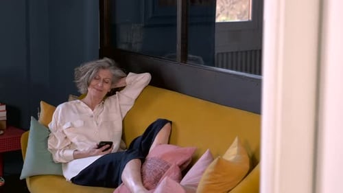 Senior womaan relxing on sofa, reading on her smart phone