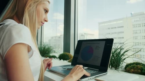 Businesswoman Working with Laptop in New Office. Side View of Woman Sitting at Table Alongside