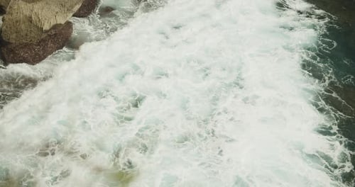 Close Up Slow Motion View of the White Sea Foam of the Ocean Waves Crashing Ashore the Rocky Beach