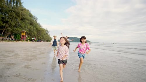 4K Asian family parents with two little daughter playing on the beach together at summer sunset.