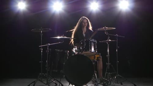 Woman Playing Drums in a Dark, Lit Setting