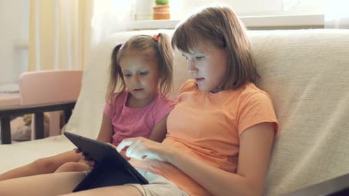 Girls Use Tablet Technology Together on Couch Indoors