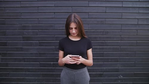 An Attractive Young Lady Wearing Glasses Using a Phone Against a Brick Wall Background. Close-up