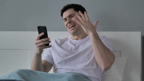 Shocked Man Looking at Mobile Phone in Bed