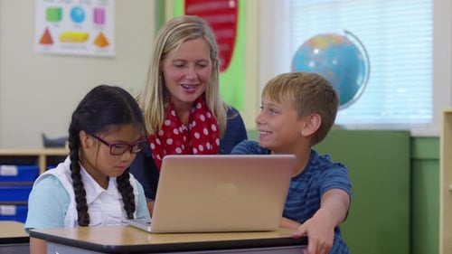 Teacher working with two students on computer project in school classroom