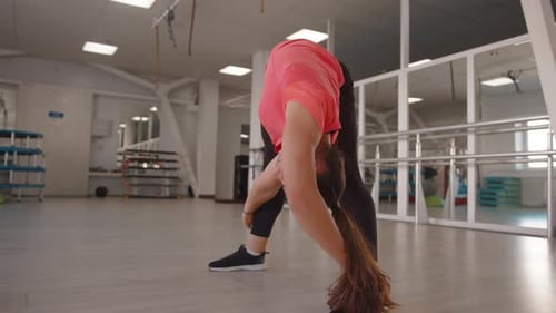 A Beautiful Young Girl Stretches After Strength Exercises in the Gym and Makes Forward Bends with a