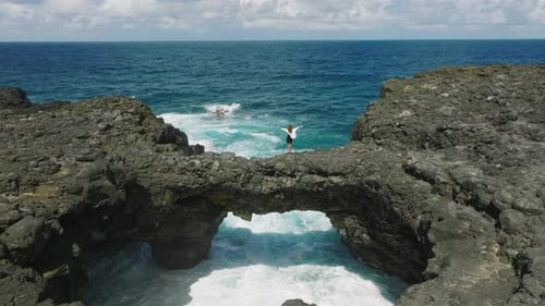 A Young Girl in a White Dress Stands on the Rocks on the Shore of the Indian Ocean