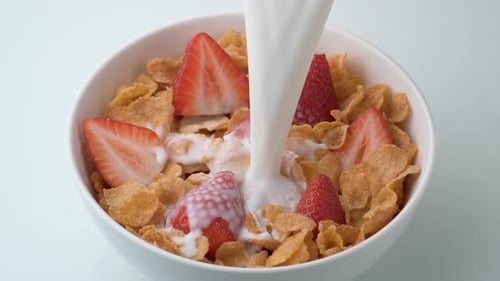 Milk being poured into bowl of cereal with strawberries