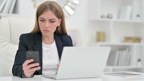 Beautiful Businesswoman Using Smartphone and Laptop in Office