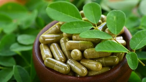 Moringa Capsules and Fresh Leaves Close Up