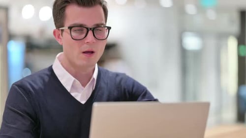 Man Coughing While Working on Laptop Indoors