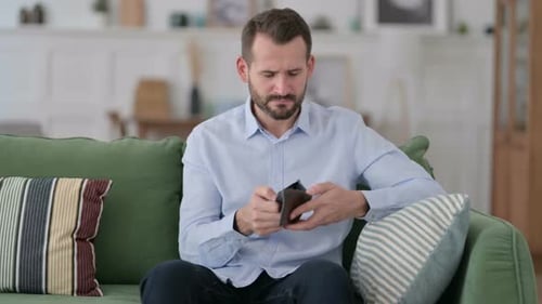 Pleite Junger Mann checkt leere Brieftasche auf Sofa