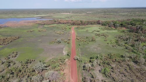 High Aerial Slow Moving drone shot of Long Straight Red Road and Green Bushland near Holmes Jungle N
