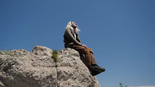 Un jeune homme hipster aux longs cheveux blonds est assis au bord d'une falaise