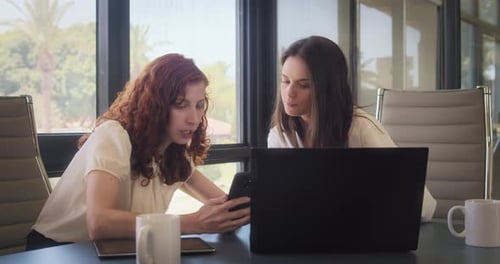 Women Collaborating at Desk Using Laptop and Phone