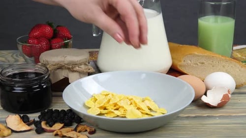 Hand Pours Corn Flakes into Bowl