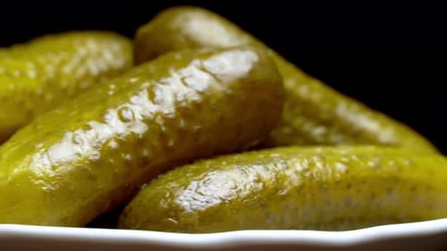 Pimply pickled cucumbers close-up on a white plate on a black background
