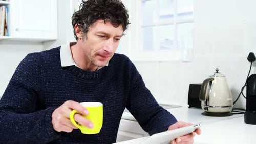 Man Using Tablet and Drinking Coffee in Kitchen