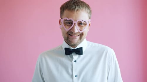 Smiling Man Wearing Heart Glasses on Pink Background