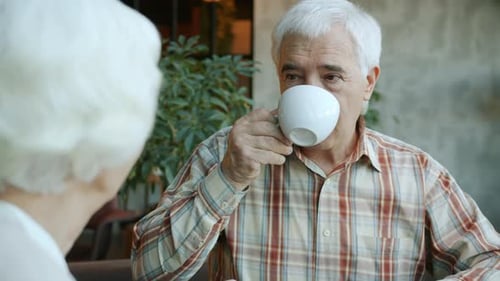 Senior Man Talking To Happy Wife and Drinking Tea Enjoying Lunch Time in Cafe