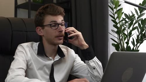 Cheerful young businessman is talking on mobile phone emotionally at modern office.
