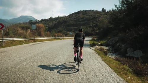 Professional road cyclist riding bicycle, pushing pedals hard, doing intense workout.