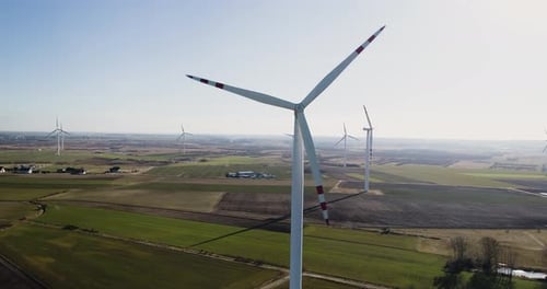 Large wind turbines with blades in field aerial view bright orange sunset blue sky wind park slow mo