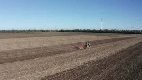 Tractor Tilling Field with Wind Turbines in Background