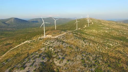 Flying above elegant ecological wind turbines on green hills