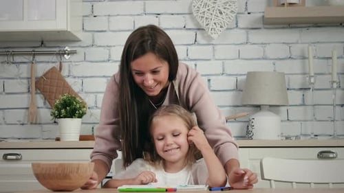 Mother Helping Child Draw Together at Kitchen Table