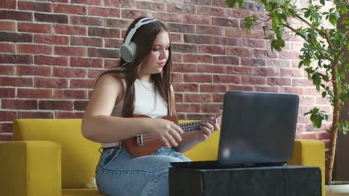Young Woman Playing Ukulele and Using Laptop