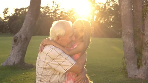 Loving Grandfather Hugging Granddaughter at Sunset in Park