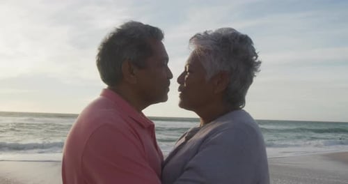 Portrait of happy hispanic senior couple kissing on beach at sunset