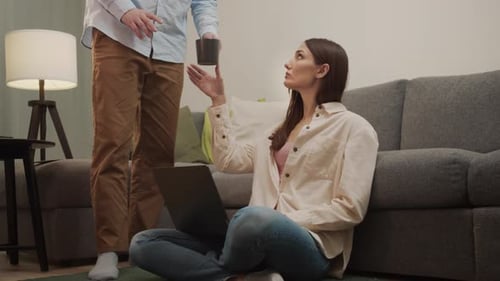 Woman Working on Laptop Receives Mug From Man