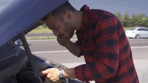 The man whose car broke down tries to fix it.