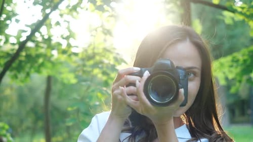 Une jolie photographe souriante et riante portant une chemise blanche fait des photos dans un parc sur un