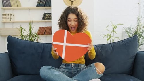 Woman Opening Heart Gift Box on Cozy Couch