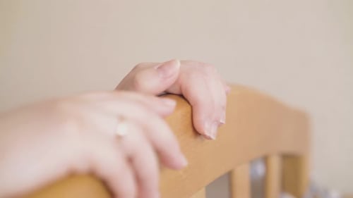 Woman's Hands Resting on Wooden Baby Crib Rail